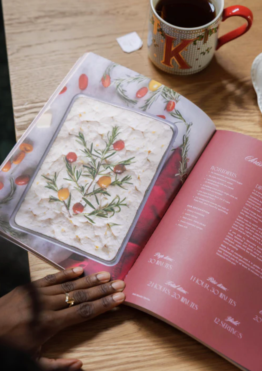 Open book with a recipe on a wooden table next to a mug.