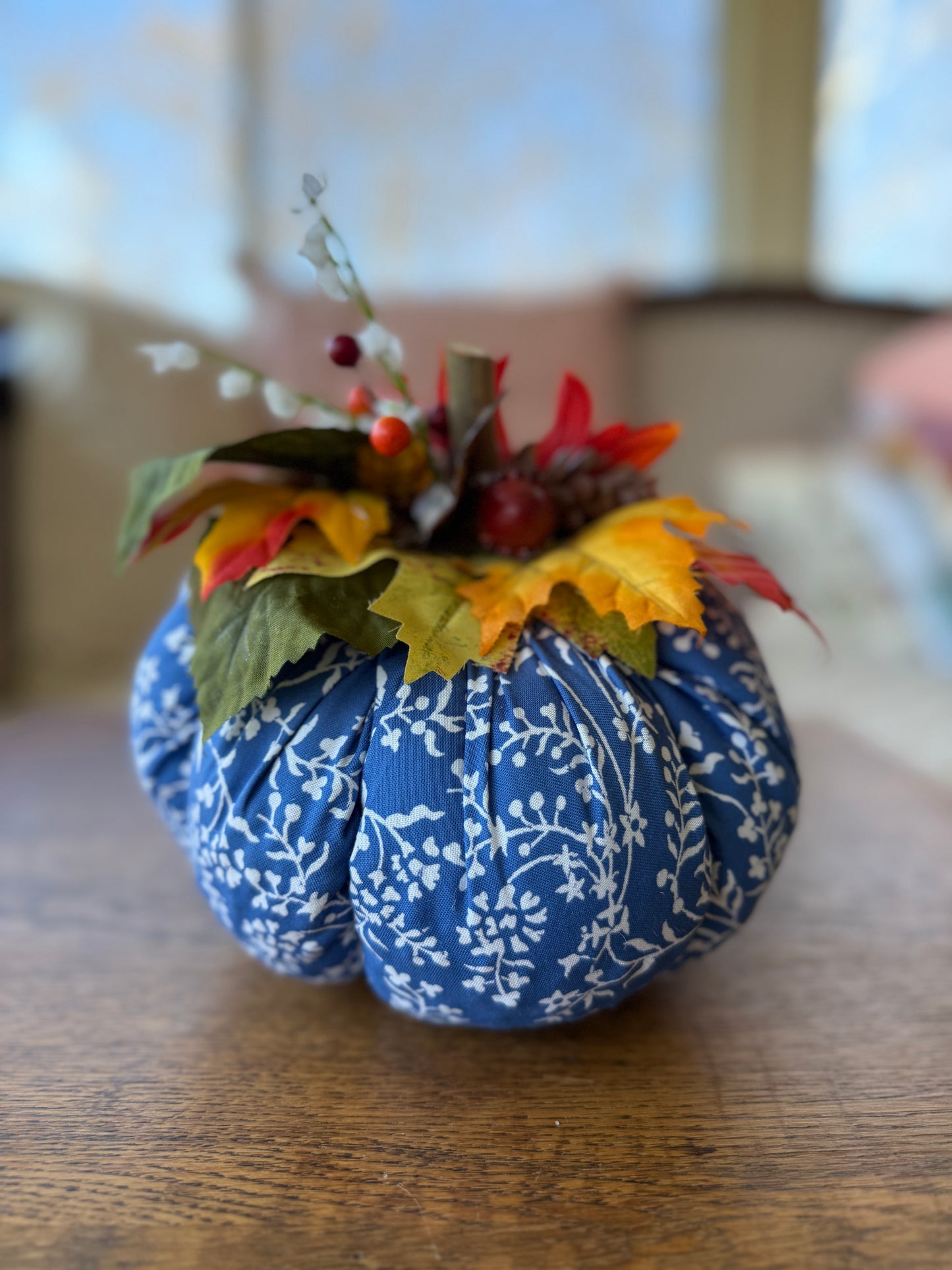 Decorative pumpkin with blue fabric wrap and autumn leaves on a wooden surface