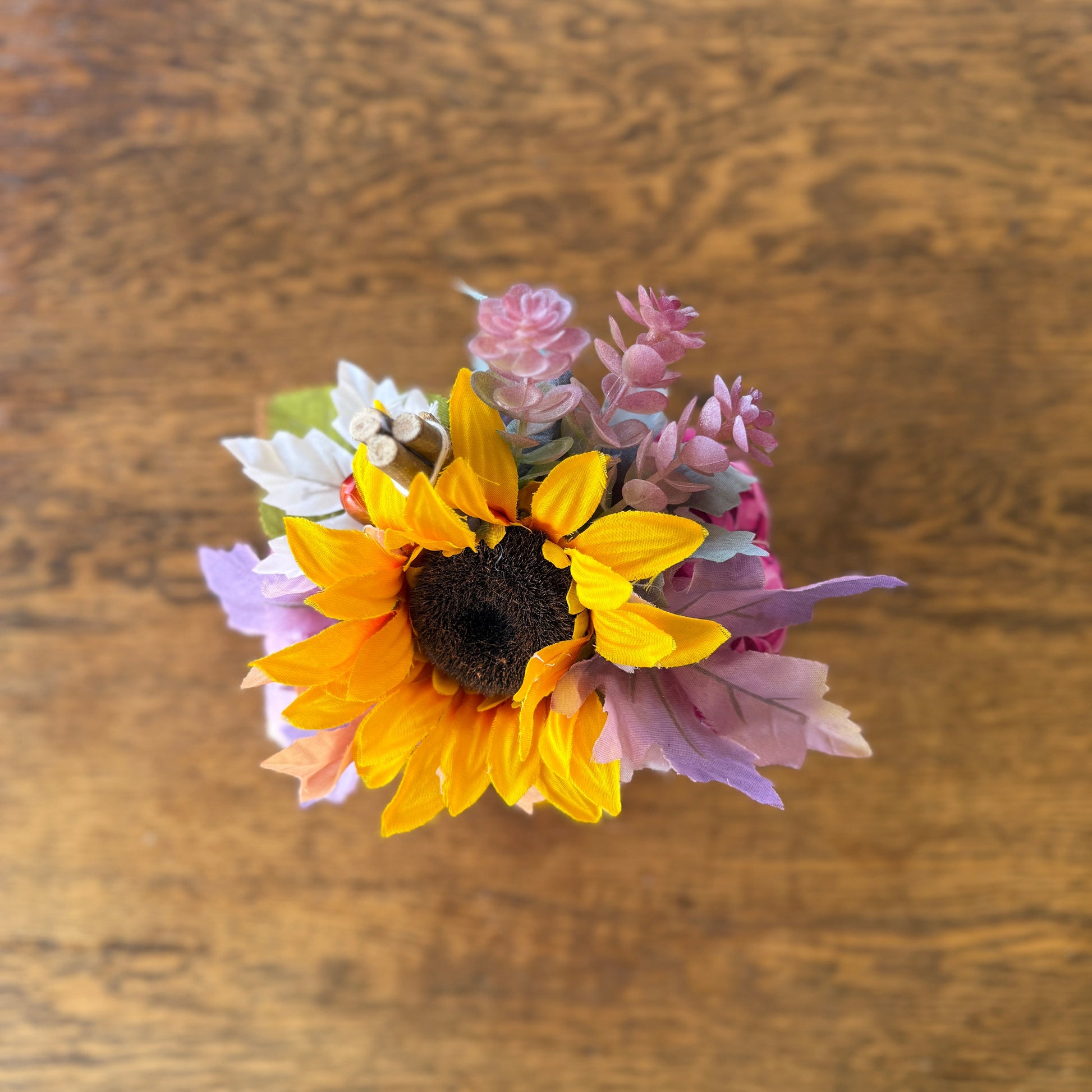 Small bouquet of flowers including sunflowers and pink flowers on a wooden surface
