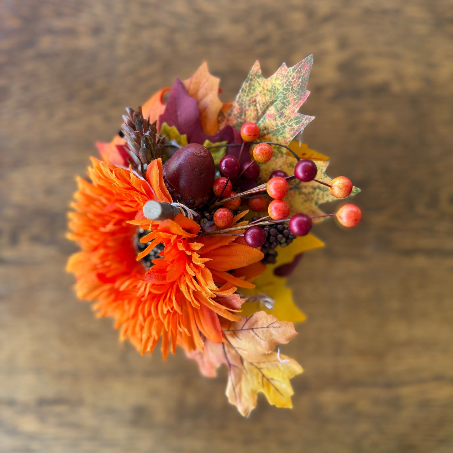 Decorative flower arrangement with orange bloom, leaves, and berries on a wooden surface