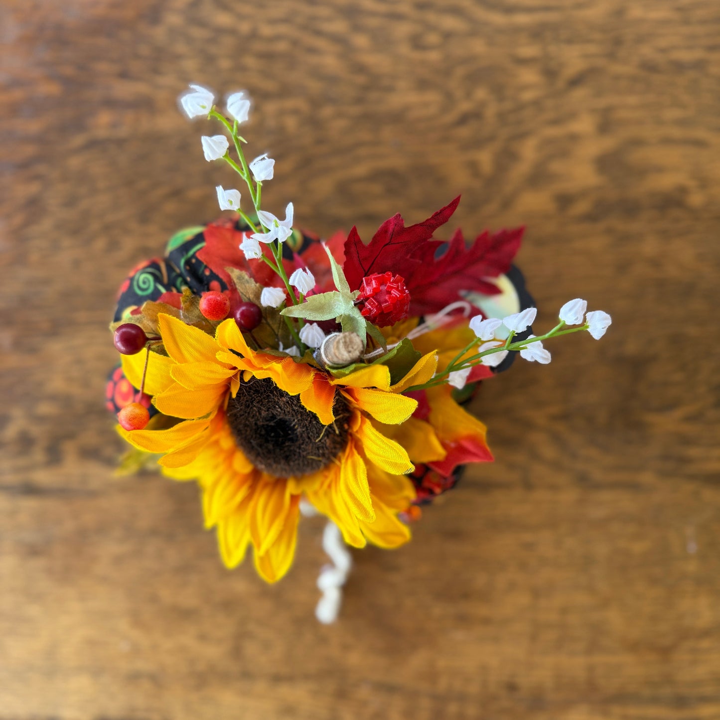 Small bouquet with sunflowers, red leaves, and white flowers on a wooden surface