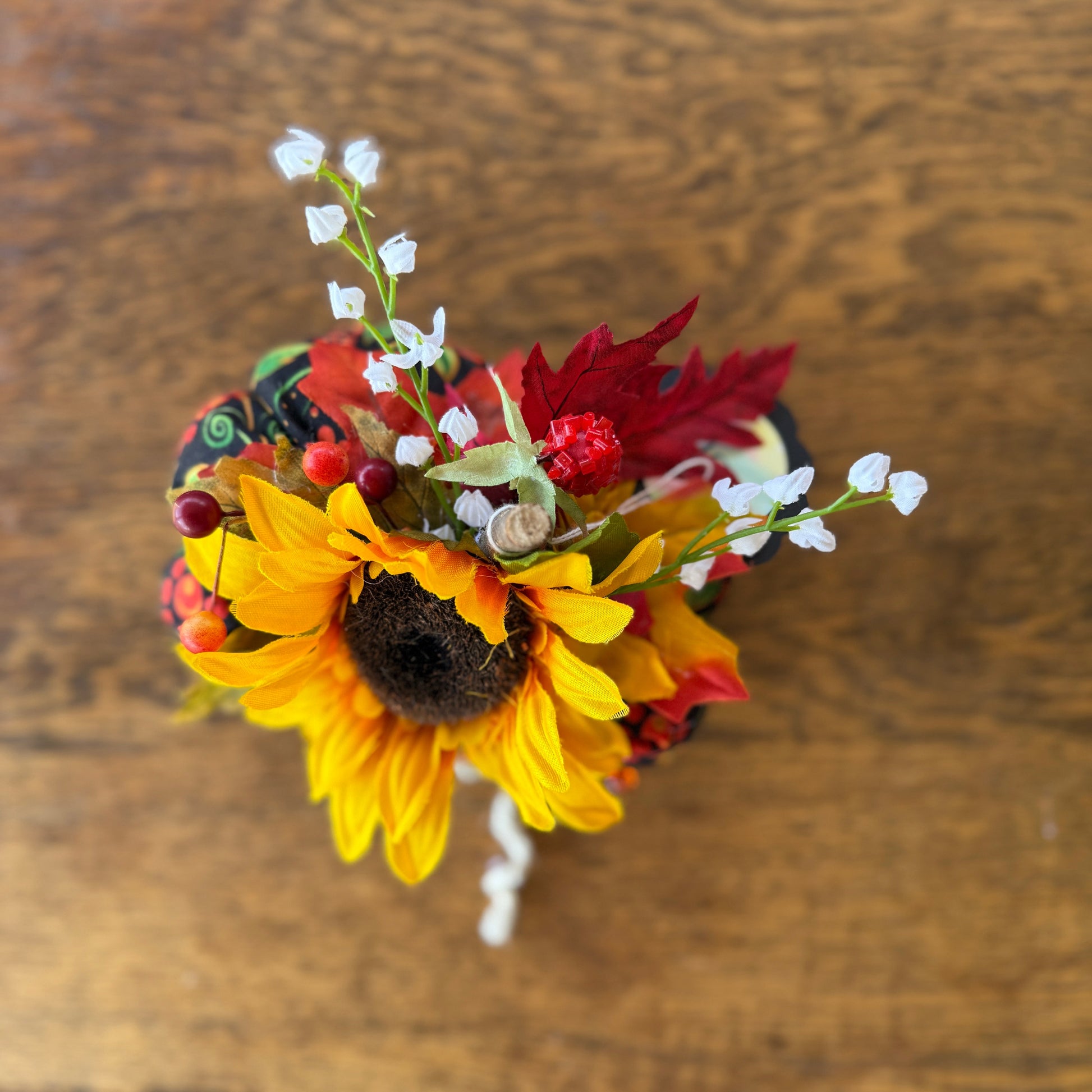 Small bouquet with sunflowers, red leaves, and white flowers on a wooden surface